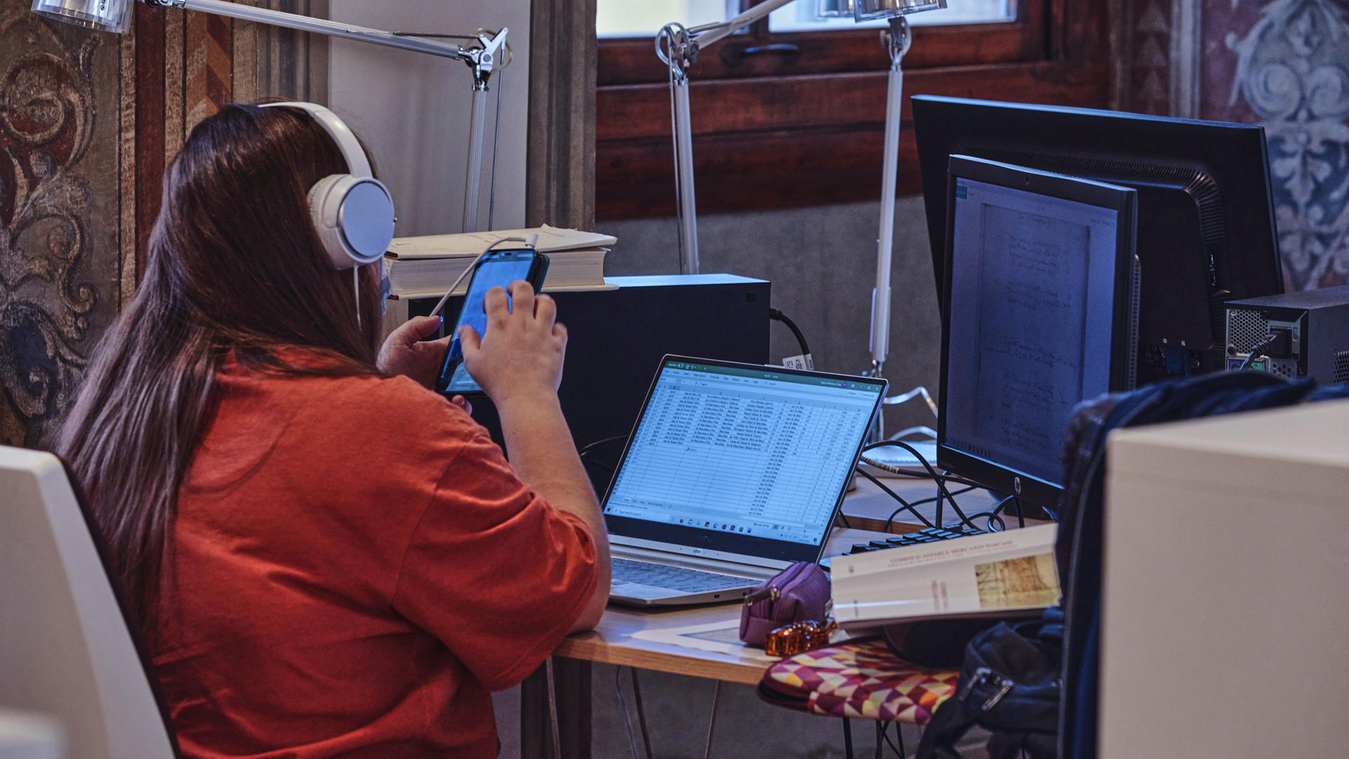 Researcher with headphones using a phone, laptop and PC. 