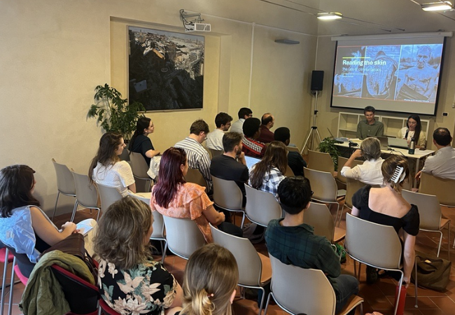 Audience seated during a library talk with speakers and presentation screen