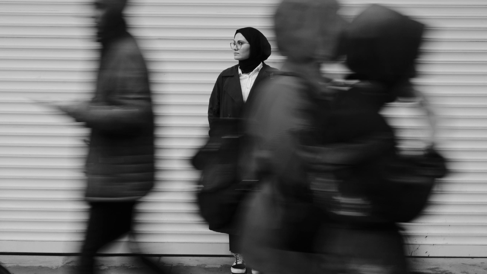 Girl wearing a hijab and glasses looks on with a hopeful expression.