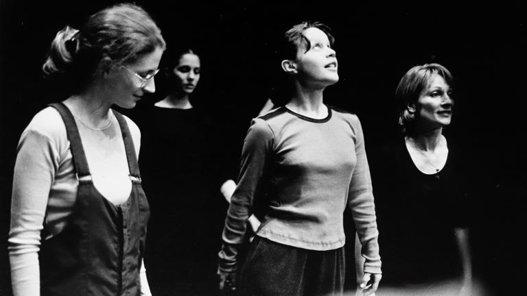 Black-and-white photograph of four women standing on a dark stage. 
