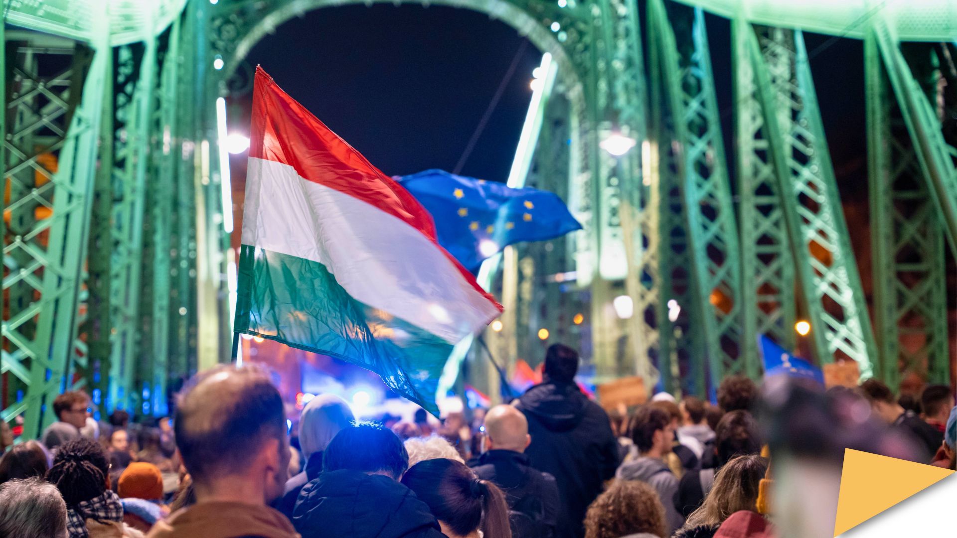Crowd gathered on a bridge in Budapest, with Hungarian and EU flags visible at night