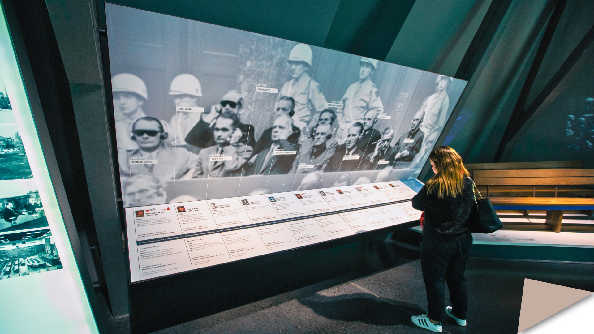 A visitor looks at a large display showing a historical video footage of the defendants at the Nuremberg trials.