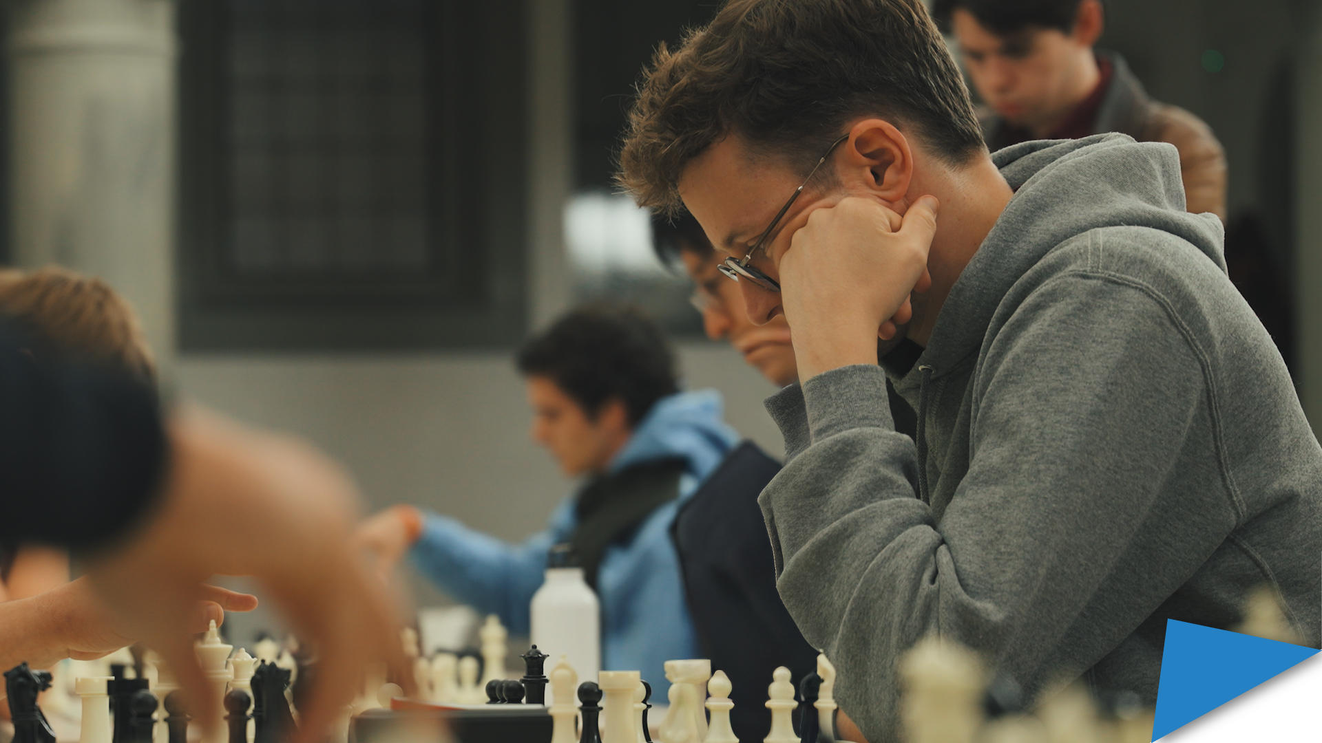 Antoine De Spiegeleir focuses on a chess match during a tournament, seated among other players in a large hall.