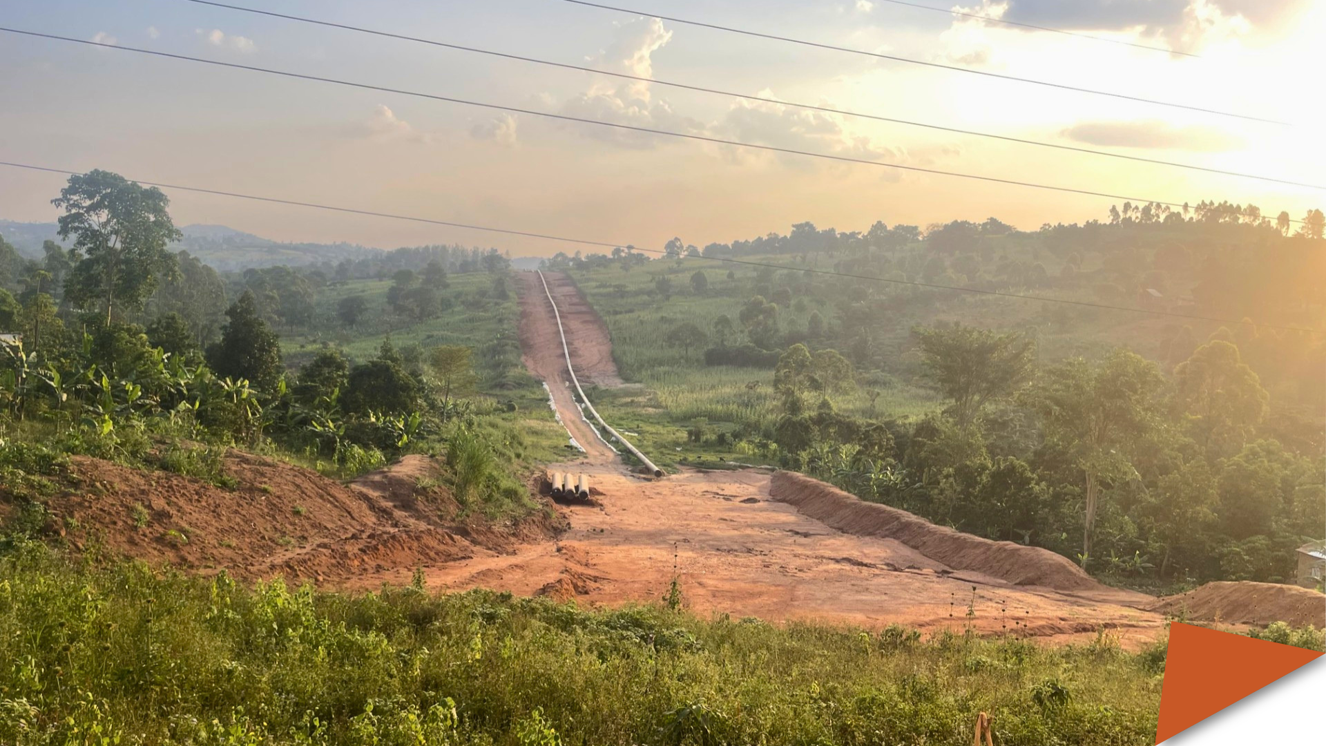 The East African Crude Oil Pipeline corridor under construction, cutting through agricultural land in Uganda, photographed at sunset.