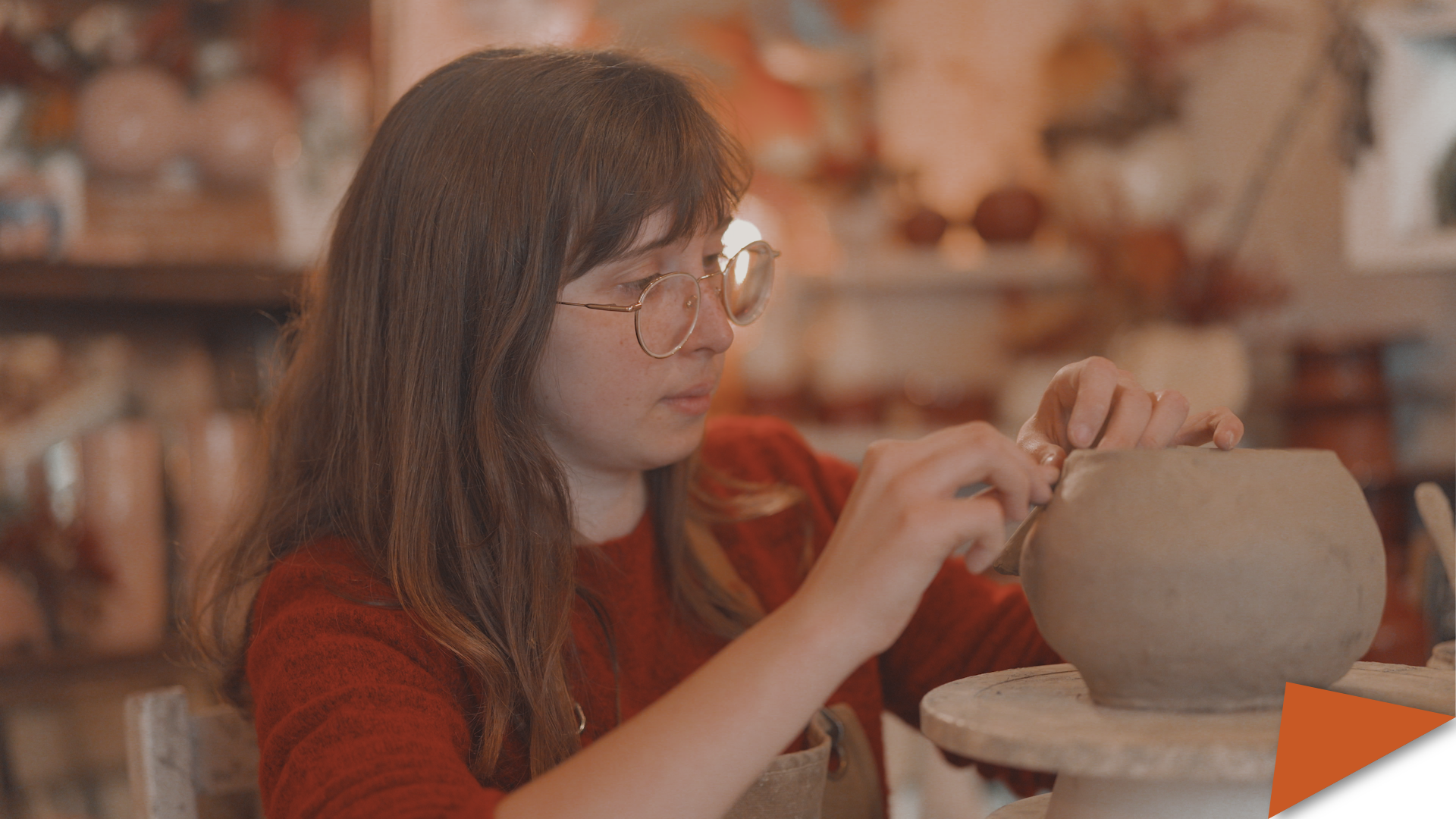 Chiara Lacroix shaping a clay pot by hand at La Cocciaia ceramic studio, with shelves of pottery visible in the background.